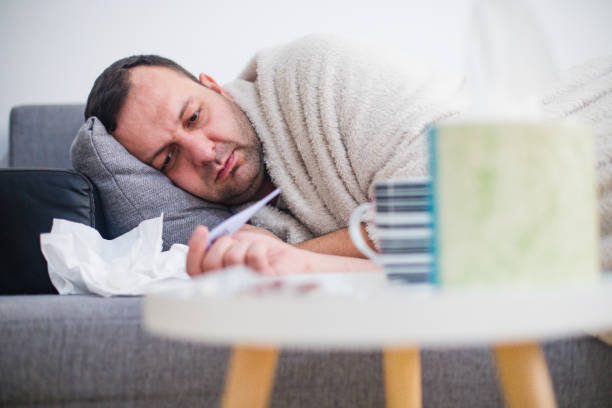 Sick man in bed checking fever with thermometer stock photo