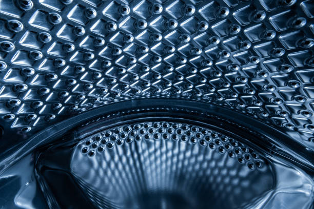 Puddle of water accumulated on the bottom of an empty washing machine drum. Wide angle view, bright, standing water, no people