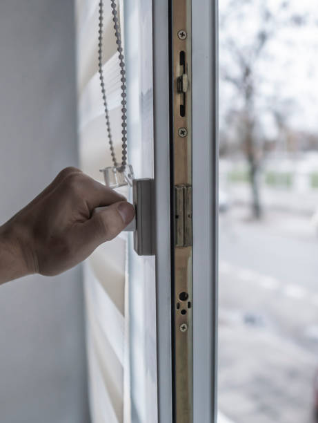 istock Man holding window handle on a plastic window with white fabric roller blinds in the living room. Close up on roll curtains indoor. 1198422257