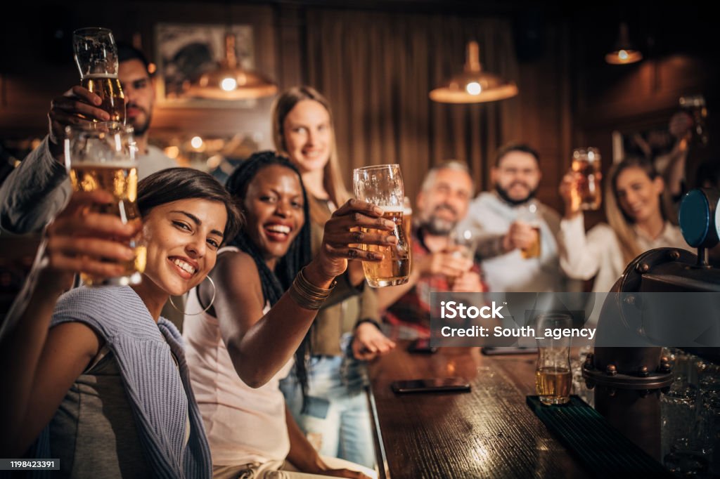 Group of friends drinking beer at the bar Multi-ethnic group of people, men and women sitting at the bar in pub, drinking beer together. Adult Stock Photo