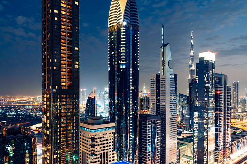 Downtown Dubai cityscape at sunset. Illuminated futuristic modern skyline and clear sky. Transitioning from day to night city lights begin to appear in the dark.