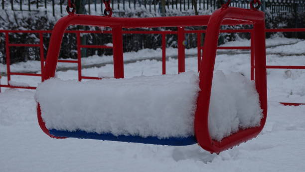 a red child seat sways in a playground filled with adhering snow. - adhering imagens e fotografias de stock