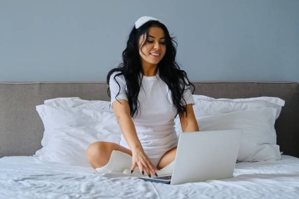 istock Beautiful brunette woman sitting in bed using laptop computer 1198427042
