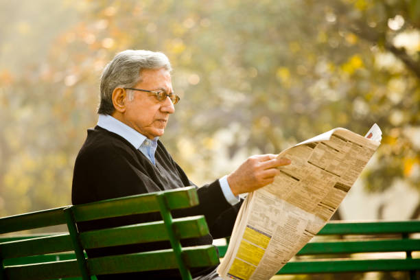 старший человек, читающих газету в парке - newspaper glasses the media reading стоковые фото и изображения