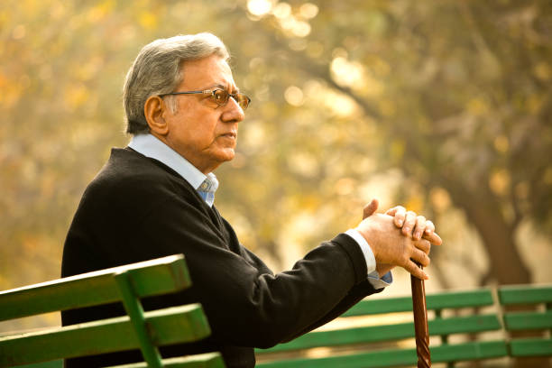 Thoughtful senior man sitting on park bench with walking cane