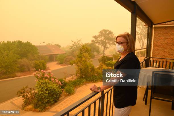 A Woman On A Balcony Wears A Face Mask To Protect Herself Against Very Dangerous Level Of Air Pollution A Thick Yellow Fog Coming From The Nearby Forest Fires Covers Canberra City Stock Photo - Download Image Now