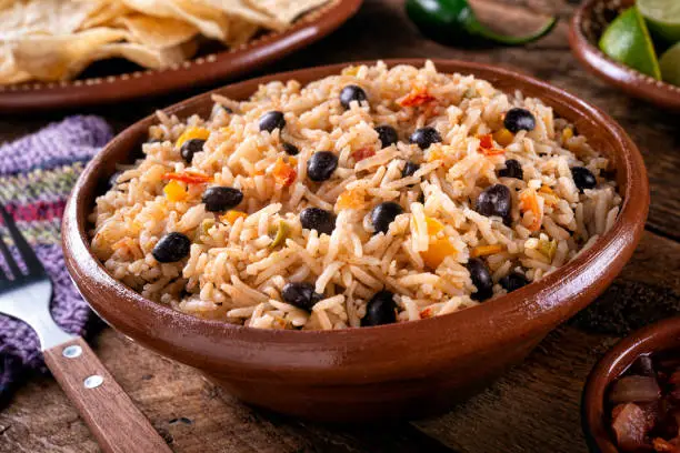 A bowl of delicious black beans and rice on a rustic table top.
