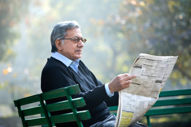 Senior man sitting on bench and reading a newspaper in the park