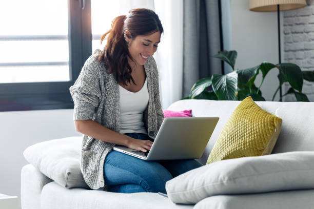 istock Pretty young woman using her laptop while sitting on sofa at home. 1198429597