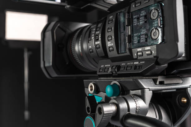 istock Side view of 4K video camera on camera tripod, audio control panel, black background 1198429795