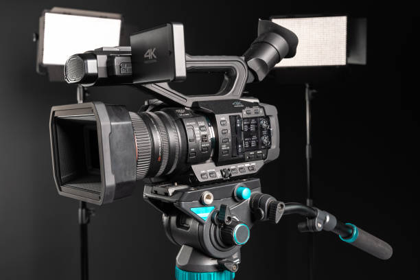 istock Professional 4K video camera on camera tripod and two lighting LED panel on black studio background 1198429819