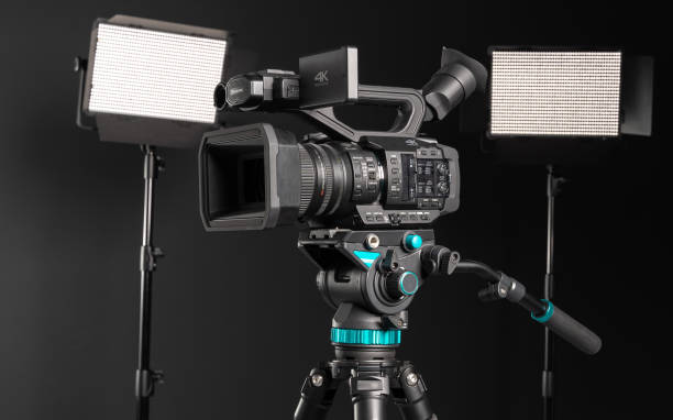 istock Professional 4K video camera on camera tripod and two lighting LED panel on black background, side view 1198429855