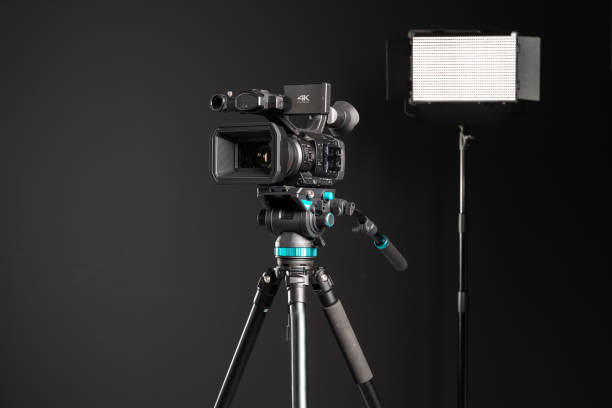 istock Professional 4K video camera on camera tripod and lighting LED panel on black background 1198429864