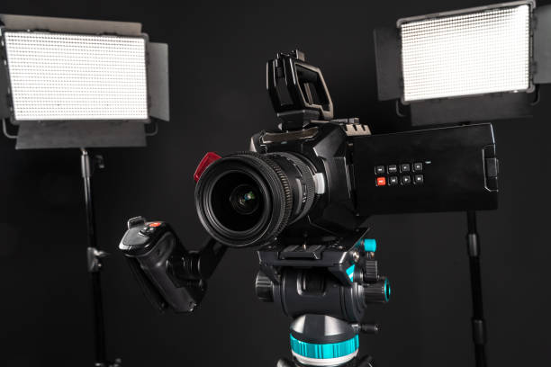 istock Professional cinema video camera on a camera tripod and one lighting LED panel on black studio background 1198429884