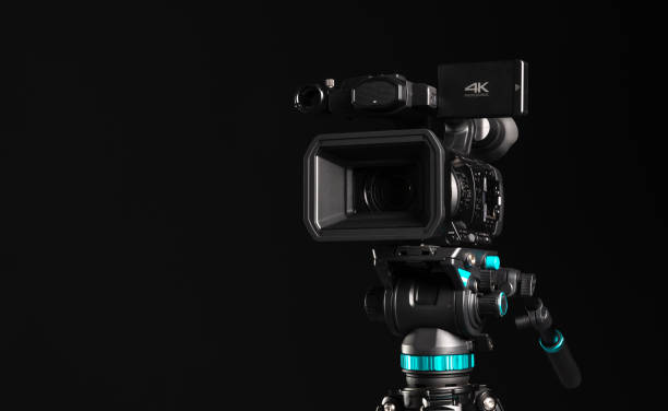 istock Professional 4K video camera on camera tripod on black background, copy space, front view 1198429971
