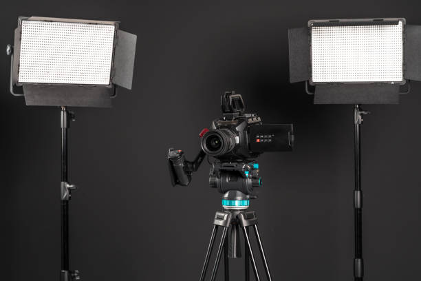 istock Professional cinema video camera on a camera tripod and one lighting LED panel on black studio background 1198429978