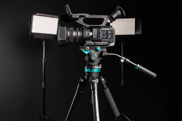 istock Side view of professional 4K video camera on camera tripod and two lighting LED panel on black studio background 1198430005