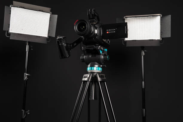 istock Professional cinema video camera on a camera tripod and two lighting LED panel on black studio background 1198430026
