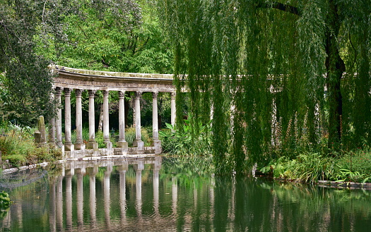 Paris, France. View of Parc Monceau with the classical corinthian columns known as Naumachia, ancient roman or greek temple style, and reflexes on water.