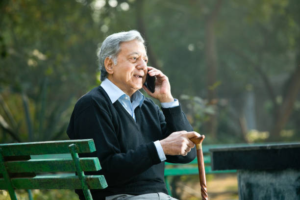 senior man watching media content using phone at park - using phone garden bench imagens e fotografias de stock