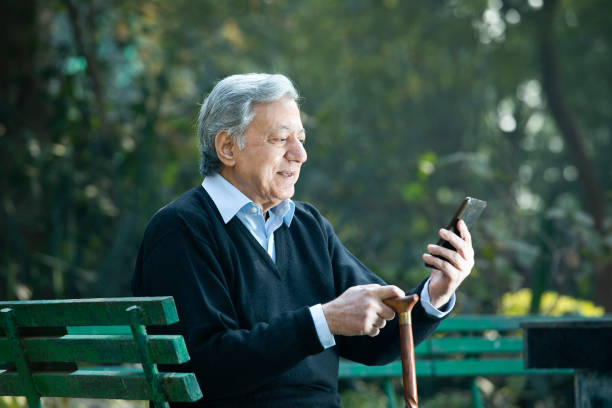 senior man watching media content using phone at park - using phone garden bench imagens e fotografias de stock