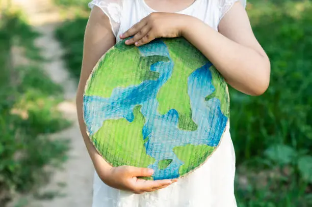 Protection and love of earth. Little girl holding planet in hands against green spring background. Earth day holiday concept. Environmental Conservation