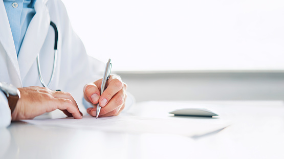 Close up of doctor signing prescription for patient