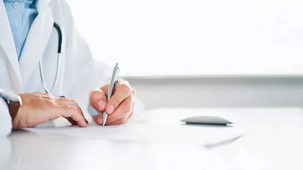 Photo of Close up of doctor signing prescription for patient