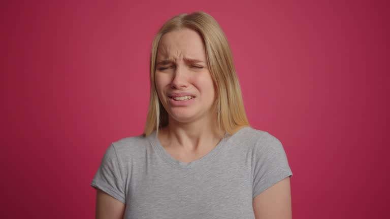 Portrait of disgusted blonde girl showing disgust for bad smell at pink wall