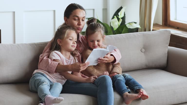 Caring young mother reading book hug cute children daughters