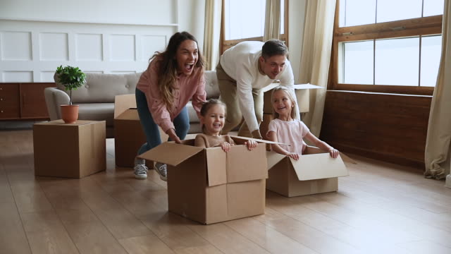 Happy parents pushing cardboard boxes with little kids, slow motion