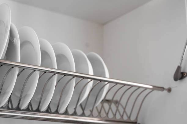 istock Dish drying metal rack with big nice white clean plates. Traditional comfortable kitchen. Open white dish draining closet with wet dishes of glass and ceramic, plates, bowls drying inside on rack. 1198451252