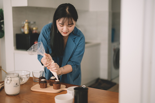 an asian chinese female piping frosting on cupcake