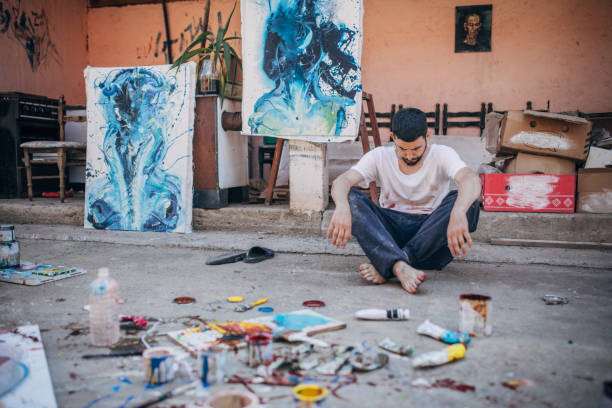 Artist-painter working on painting outdoors with art supplies around him
