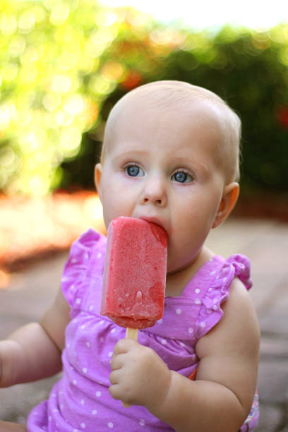 Cute Baby Girl Eating Frozen Fruit Popsicle A cute 10 month old baby girl is eating a srawberry frozen fruit popsicle outside on a summer day. 10 11 years photos stock pictures, royalty-free photos & images
