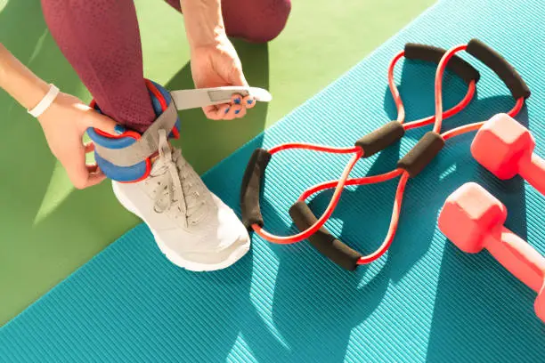 Photo of Woman putting on ankle wights before she starts a workout in a gym, health and fitness concept