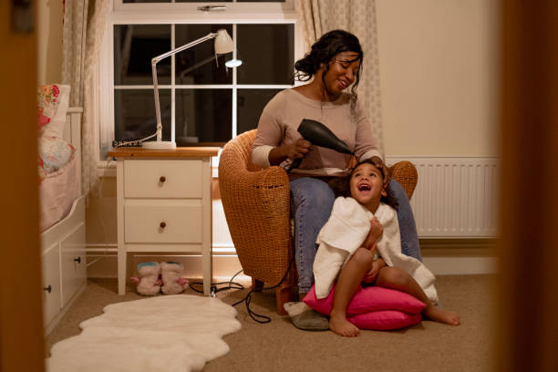 Fun Bedtime Routine A mother drying her daughter's hair with a hairdryer. They are sitting in the girl's bedroom together. turning on lamp stock pictures, royalty-free photos & images