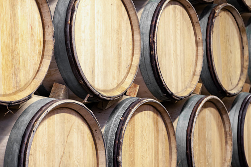 Wooden wine oak barrels stacked in straight rows in order, old cellar of winery, vaults. Concept brewery background, professional degustation, winelover, sommelier travel, copyspace, place for text