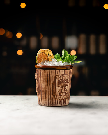 A tiki cocktail in a classic tiki cup. The Mai Tai cocktail with mint sprig and a dried lime and lemon wheel