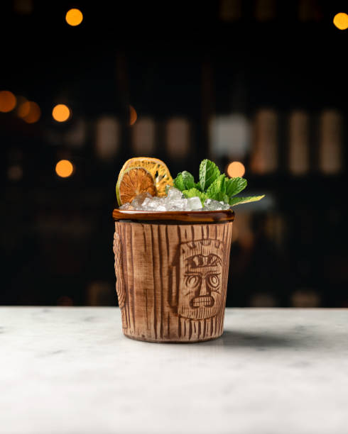 A tiki cocktail, mai tai, in a classic tiki cup A tiki cocktail in a classic tiki cup. The Mai Tai cocktail with mint sprig and a dried lime and lemon wheel mai tai stock pictures, royalty-free photos & images