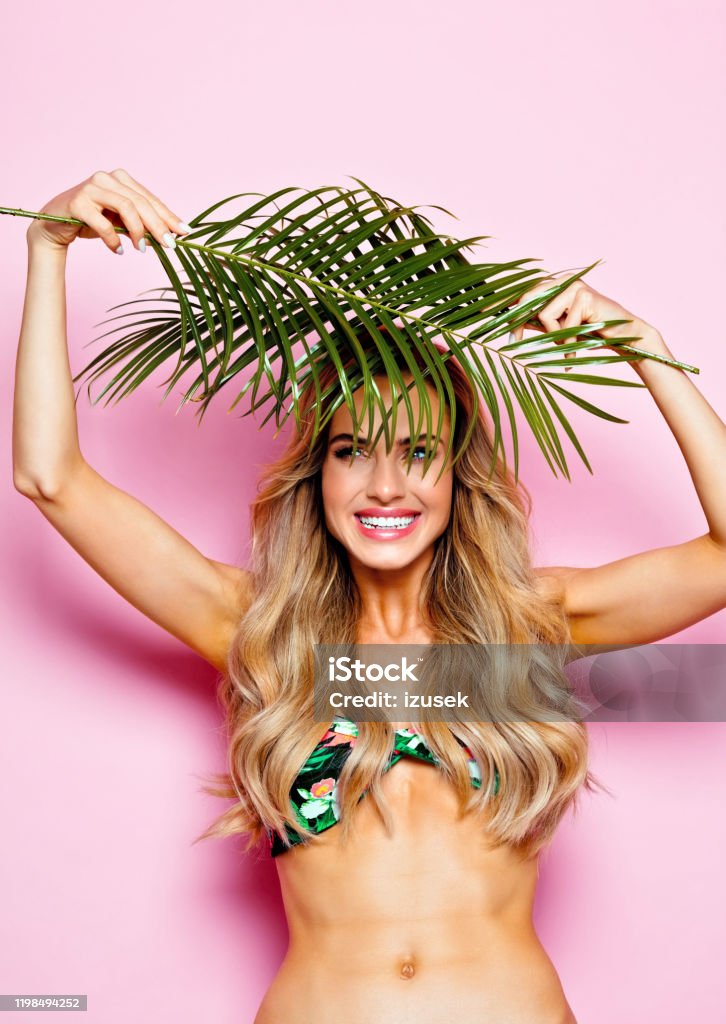 Summer portrait of young blonde woman in swimsuit Glamour portrait of beautiful long hair young woman wearing floral swimsuit, holding palm leaves. Studio shot on pink background. 25-29 Years Stock Photo