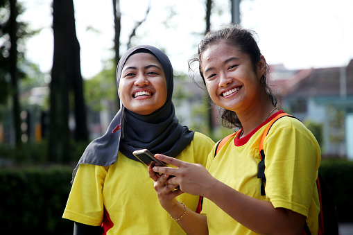 Two Muslim teenage girls using smartphone cheerfully and gearing up for Chinese New Year lion dance performance in Kuala Lumpur, Malaysia.
