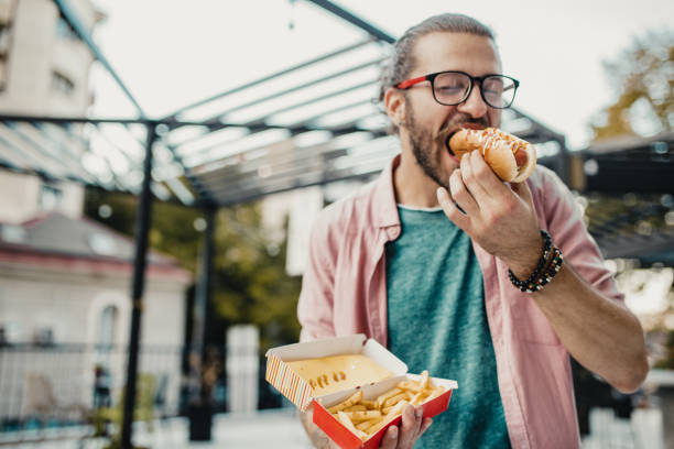 junger mann isst hot dog - breakfast eating people teens stock-fotos und bilder