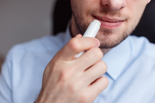 Man applying hygienic lipstick on lips to revive chapped lips and avoid dry, closeup. Man use protective cosmetics for care