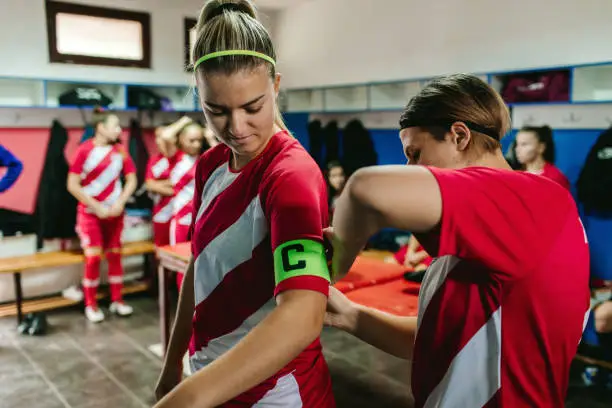 Female soccer player adjusting "captain" arm band to her teammate.