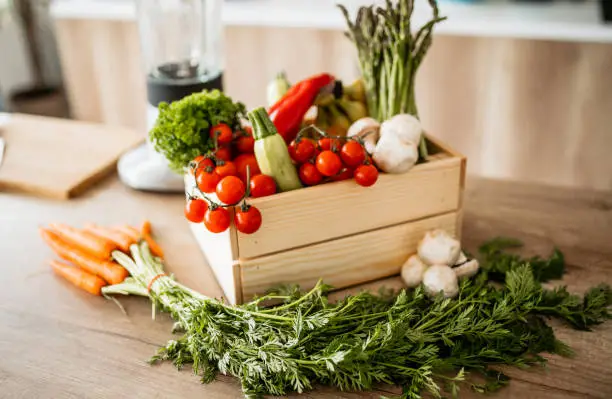 Photo of Pine box full of colorful fresh vegetables and fruits on a kitchen counter