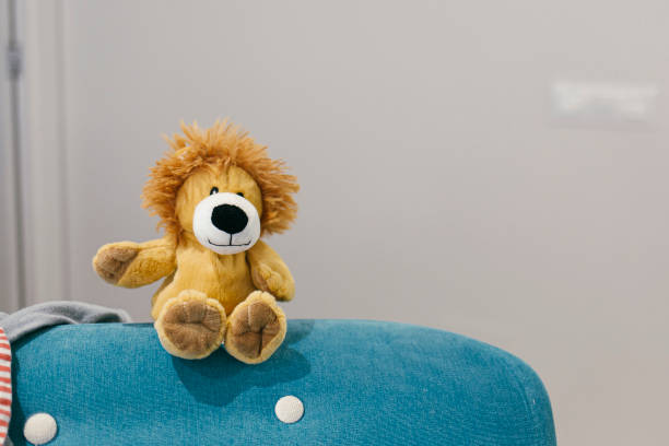Pluff bear toy waving hello sitting on a sofa on a grey background