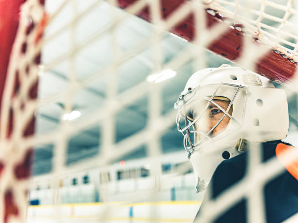 Young Caucasian male Pro Hockey goalie at the training at the hockey arena. View from behind the goal net.