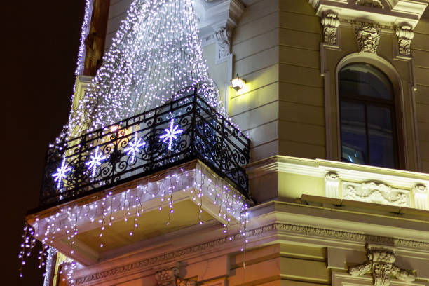 A low angle perspective of a corner building adorned with glowing golden festive lights. The architectural details are enhanced by the warm illumination, creating a celebratory and inviting ambiance.
