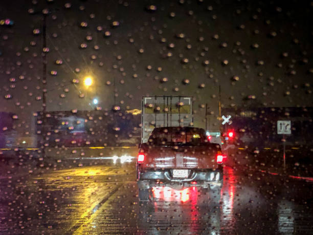 Dangerious Stop at a Railroad crossing at night in the rain A semi-truck and a pickup truck are stopped at an active railroad crossing. The image is photographed through a rainy car window. Drops of water abound in this night time shot. truck rain stock pictures, royalty-free photos & images